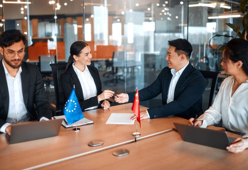 The flags of China and the European Union are on the table during negotiations between diplomats and businessmen. Representatives discuss relations between countries, signing a treaty.