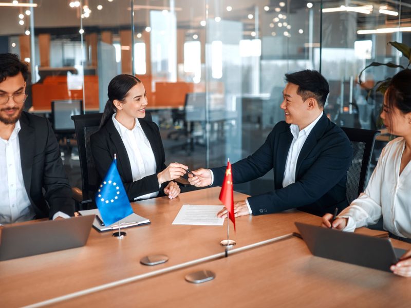 The flags of China and the European Union are on the table during negotiations between diplomats and businessmen. Representatives discuss relations between countries, signing a treaty.